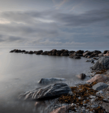 Stenar vid en lugn kustområde med molnig himmel ovanför.