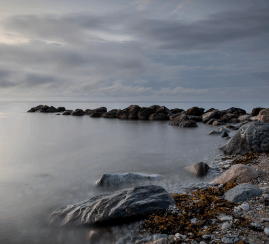 Stenar vid en lugn kustområde med molnig himmel ovanför.